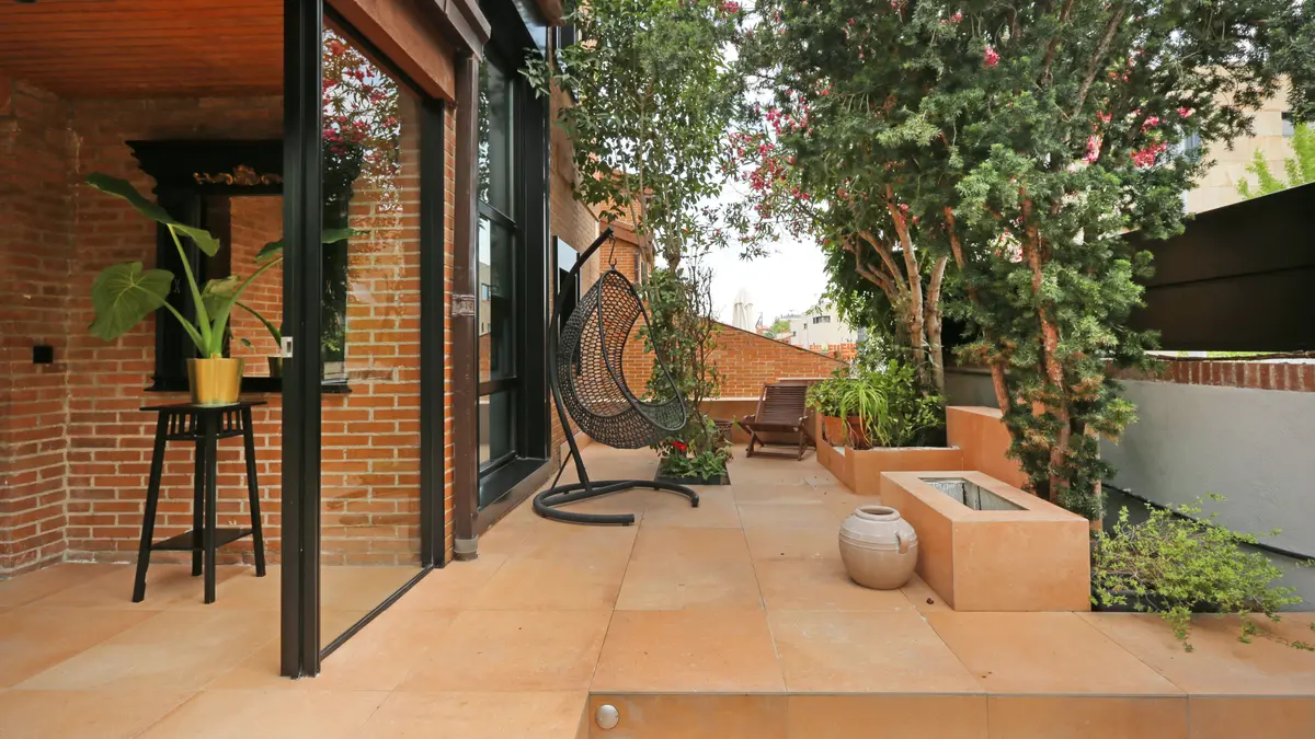 Patio con suelo de barro, jardineras y sillón colgante.